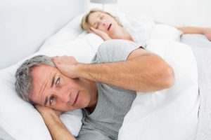 Man covering ears next to snoring woman