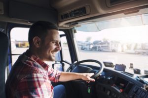 Inside shot of man in plaid smiling while driving a truck